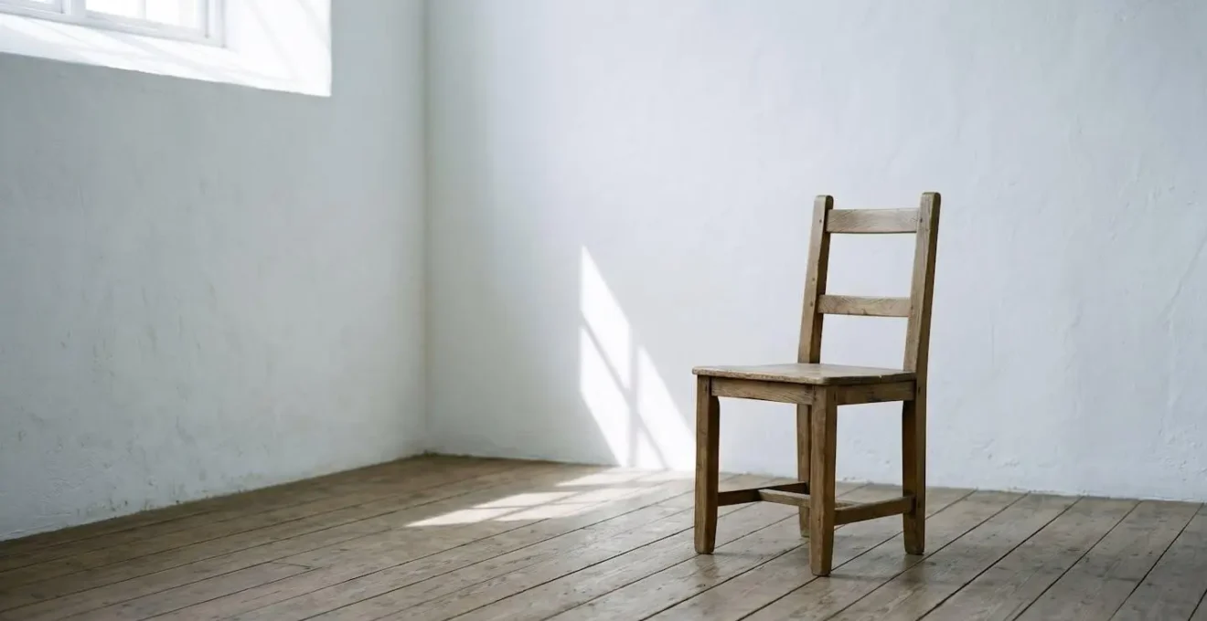 A single chair positioned in corner of empty minimalist room with dramatic natural light casting long shadows, symbolizing social withdrawal and the urge to hide