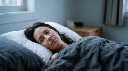 Person lying awake in dimly lit bedroom during early morning hours experiencing sleep maintenance insomnia