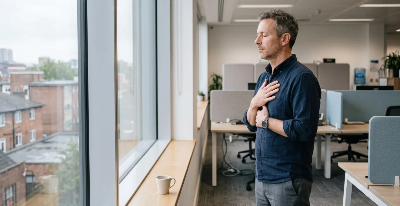 A man practises a slow breathing exercise by a window in a modern office break area.